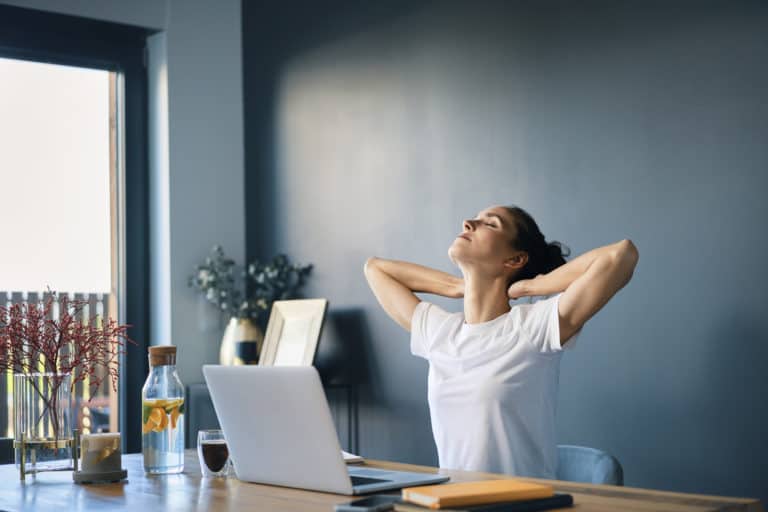 Tired businesswoman with hands behind head sitting at desk in home office